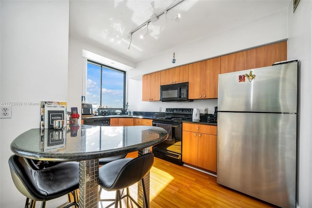 kitchen with a breakfast bar area, black appliances, light wood-type flooring, kitchen peninsula, and sink