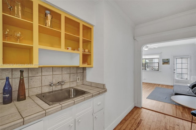 kitchen with sink, white cabinetry, ornamental molding, light hardwood / wood-style floors, and tile countertops