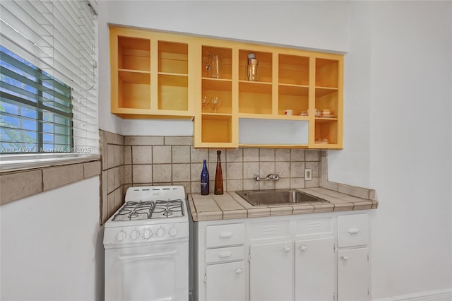 kitchen featuring sink, gas range gas stove, backsplash, white cabinets, and tile countertops