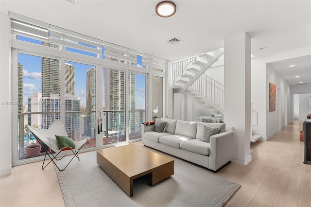 living room with baseboards, visible vents, wood finished floors, stairs, and a wall of windows