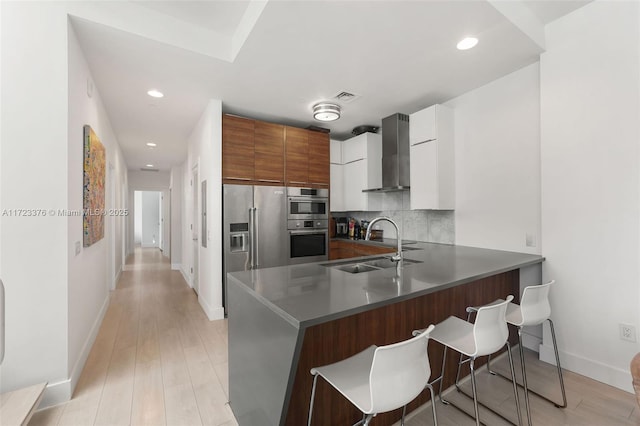 kitchen with a breakfast bar area, a peninsula, high end fridge, wall chimney exhaust hood, and tasteful backsplash