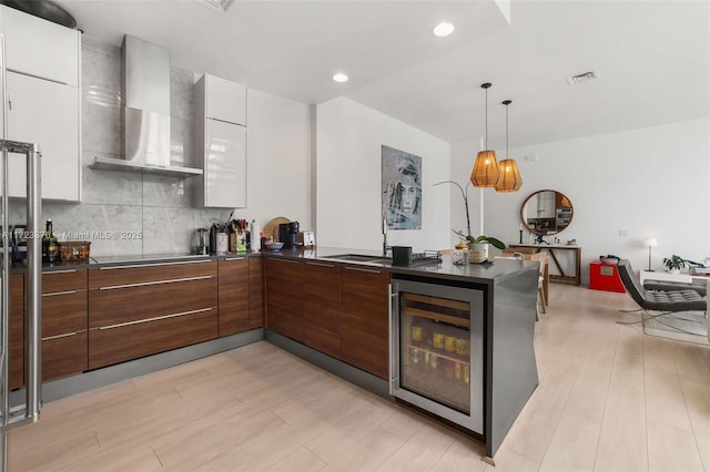 kitchen with visible vents, modern cabinets, wine cooler, wall chimney range hood, and backsplash