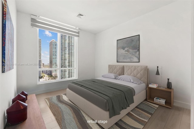 bedroom with multiple windows, wood finished floors, visible vents, and baseboards