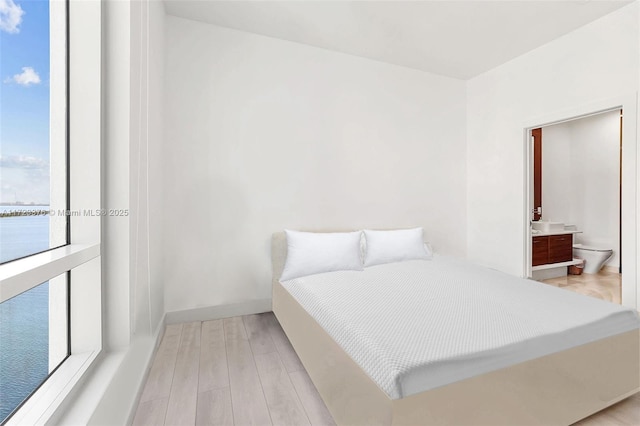 bedroom featuring light wood-type flooring, a water view, baseboards, and ensuite bathroom