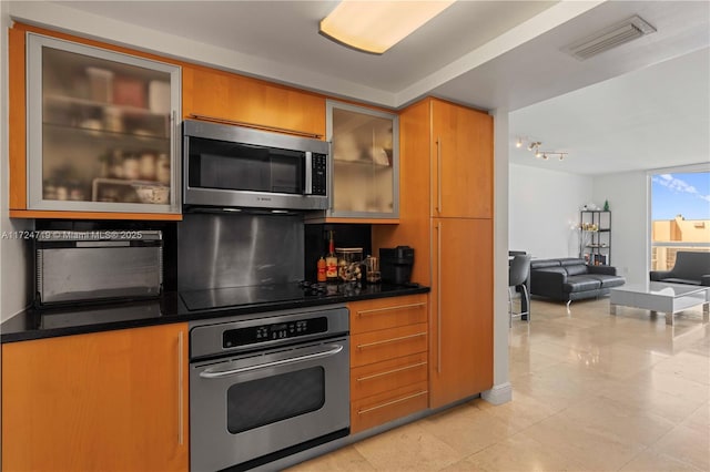 kitchen with dark countertops, light tile patterned flooring, glass insert cabinets, appliances with stainless steel finishes, and visible vents