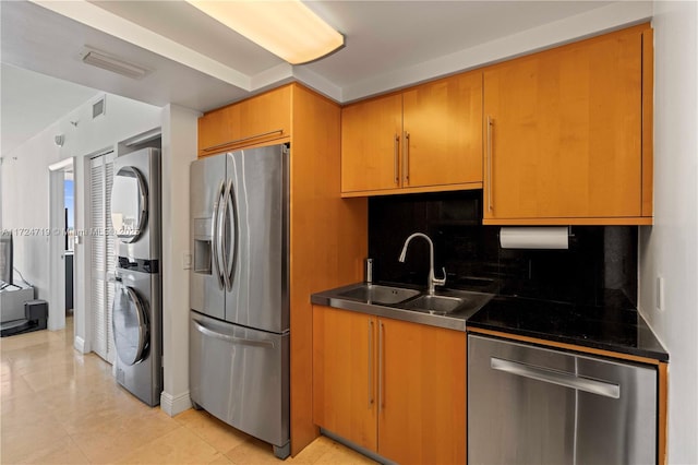 kitchen featuring stainless steel appliances, stacked washer and dryer, a sink, visible vents, and dark countertops