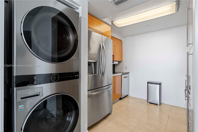 kitchen featuring stainless steel appliances, stacked washer / drying machine, light countertops, brown cabinetry, and baseboards