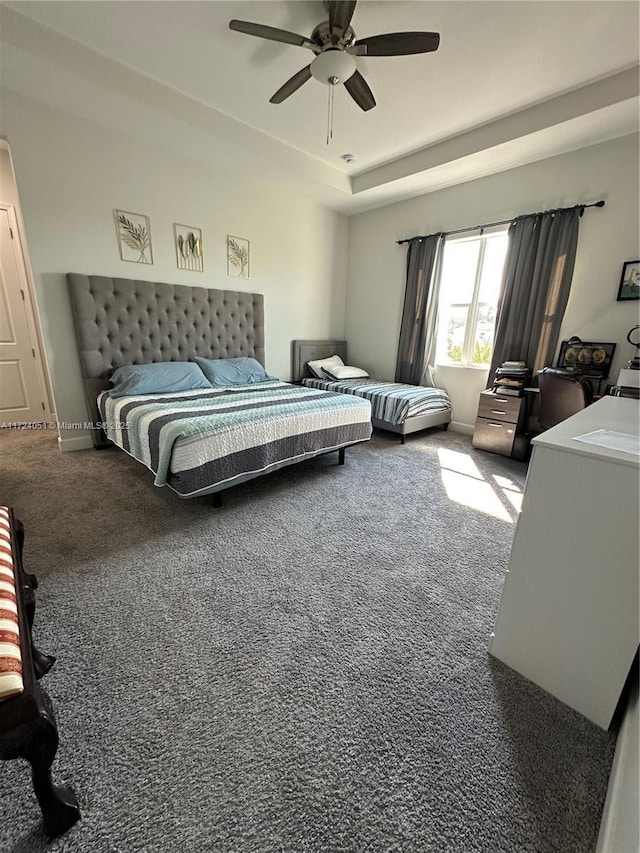 carpeted bedroom with ceiling fan and a raised ceiling