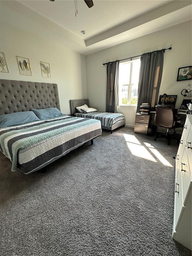 bedroom featuring dark carpet, a raised ceiling, and ceiling fan