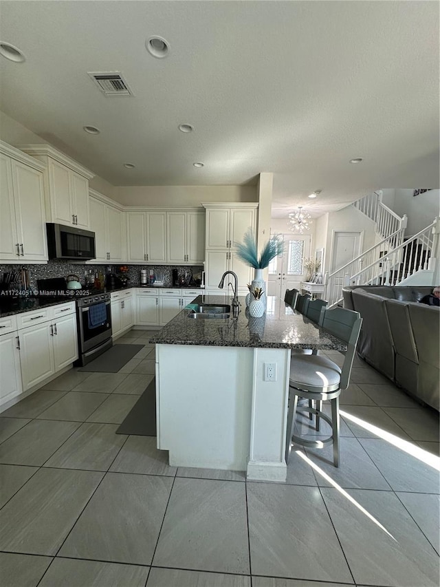 kitchen with sink, gas range, a center island with sink, dark stone countertops, and white cabinets