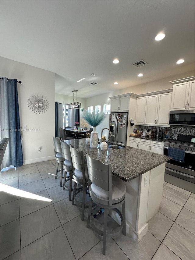 kitchen with a large island with sink, white cabinetry, appliances with stainless steel finishes, and a breakfast bar area