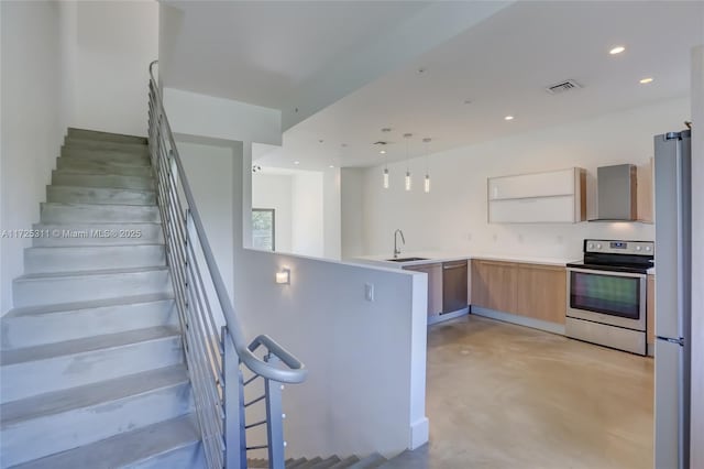 interior space with appliances with stainless steel finishes, light brown cabinetry, decorative light fixtures, kitchen peninsula, and wall chimney range hood