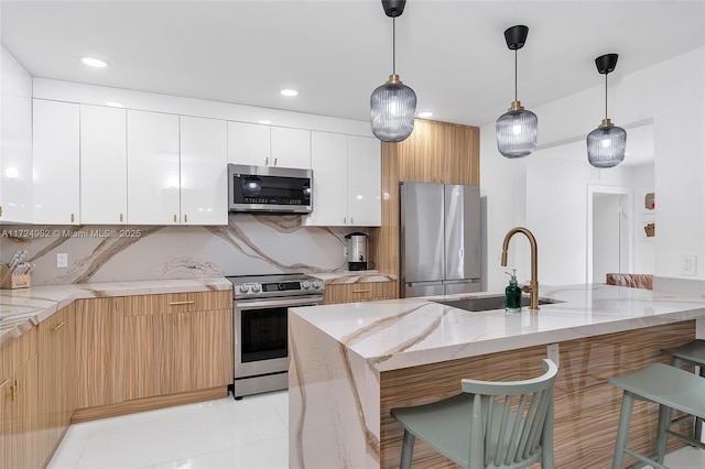 kitchen featuring stainless steel appliances, light stone counters, decorative backsplash, white cabinets, and sink