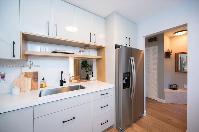 kitchen with light wood-type flooring, decorative backsplash, stainless steel refrigerator with ice dispenser, sink, and white cabinetry