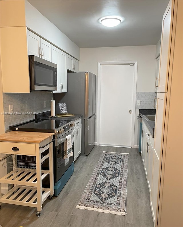 kitchen with white cabinets, stainless steel appliances, backsplash, and wood-type flooring