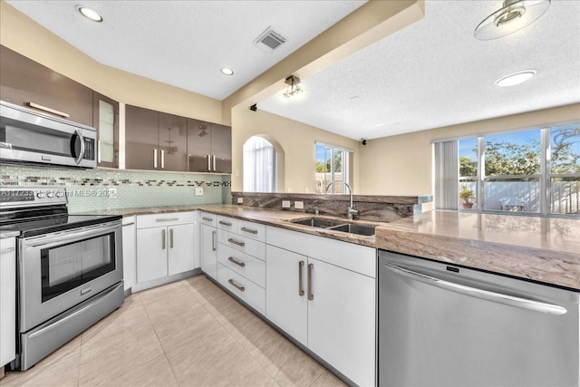 kitchen with a textured ceiling, stainless steel appliances, decorative backsplash, white cabinetry, and sink