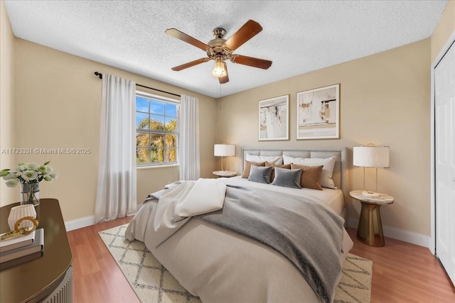 bedroom with a textured ceiling, ceiling fan, and light hardwood / wood-style floors