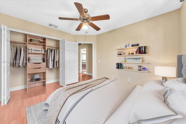 bedroom featuring light wood-type flooring, ceiling fan, a closet, and a textured ceiling