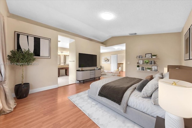 bedroom featuring a textured ceiling, vaulted ceiling, ensuite bath, and hardwood / wood-style flooring