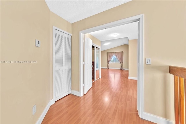 hall featuring a textured ceiling, hardwood / wood-style floors, and lofted ceiling