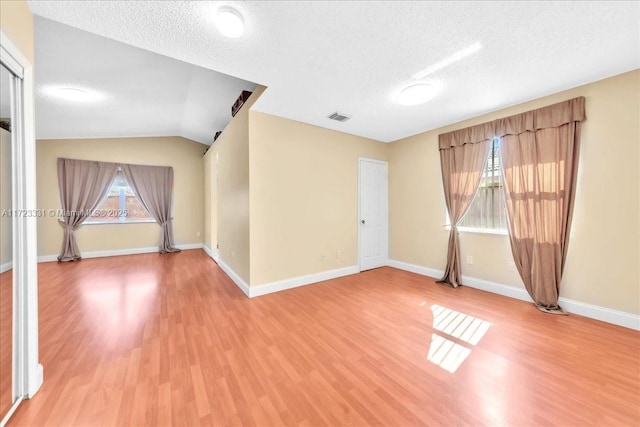 empty room with lofted ceiling, hardwood / wood-style flooring, a textured ceiling, and a healthy amount of sunlight