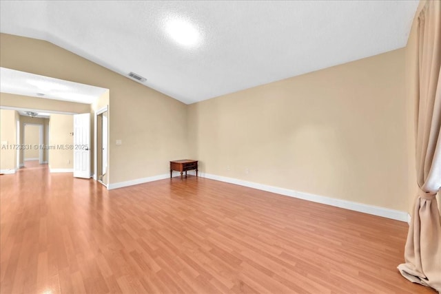 spare room featuring lofted ceiling, light wood-type flooring, and a textured ceiling