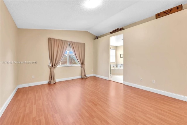 empty room featuring a textured ceiling, light wood-type flooring, and lofted ceiling