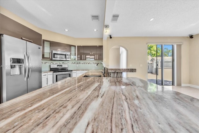 kitchen featuring sink, a textured ceiling, kitchen peninsula, decorative backsplash, and appliances with stainless steel finishes