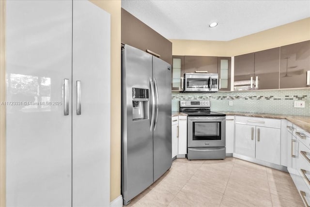 kitchen featuring white cabinetry, light tile patterned floors, backsplash, light stone countertops, and appliances with stainless steel finishes