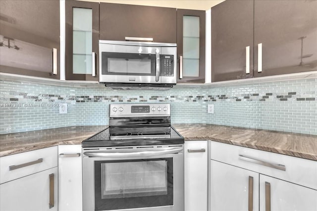 kitchen featuring dark stone counters, appliances with stainless steel finishes, white cabinetry, and decorative backsplash