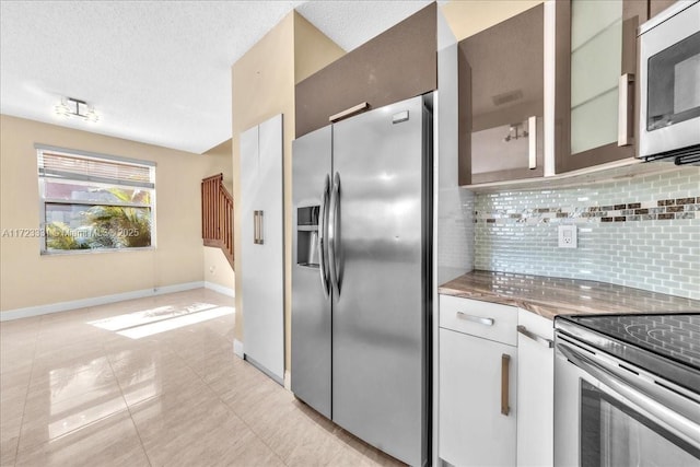 kitchen featuring a textured ceiling, decorative backsplash, white cabinetry, appliances with stainless steel finishes, and light tile patterned flooring