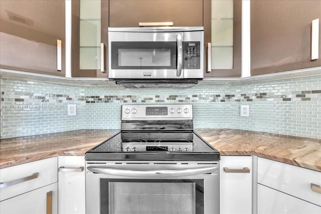 kitchen with stainless steel appliances, light stone countertops, white cabinetry, and decorative backsplash