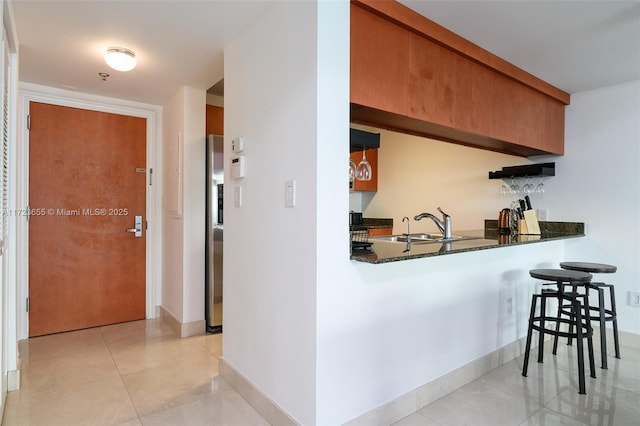 kitchen featuring sink, dark stone countertops, light tile patterned floors, kitchen peninsula, and stainless steel fridge with ice dispenser