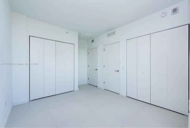 unfurnished bedroom with two closets and light tile patterned floors