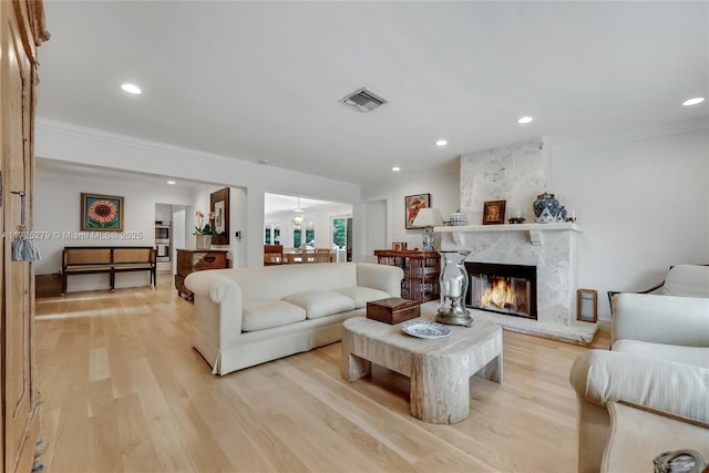 living room with a high end fireplace, ornamental molding, and light hardwood / wood-style flooring