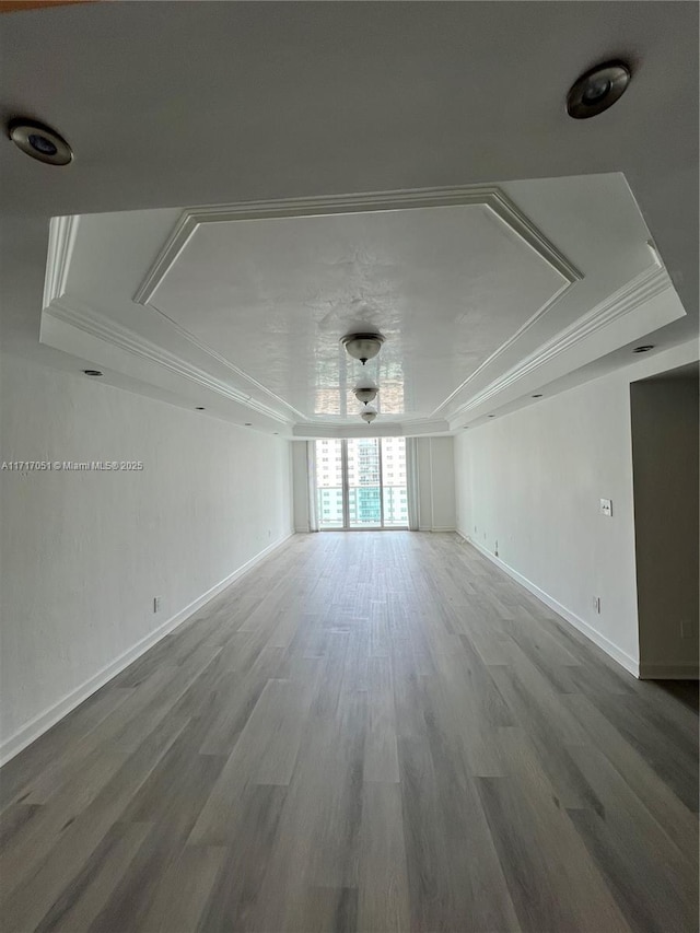 unfurnished room with a raised ceiling, ornamental molding, and hardwood / wood-style floors