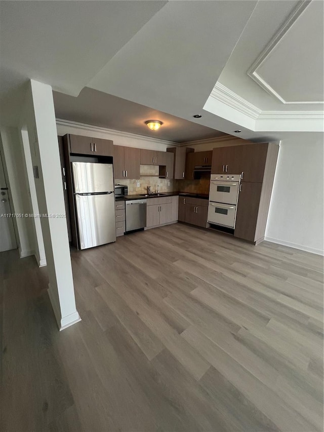 kitchen featuring appliances with stainless steel finishes, light hardwood / wood-style floors, a tray ceiling, sink, and backsplash