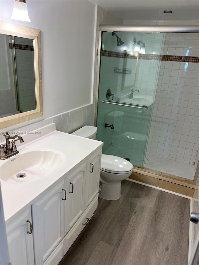 bathroom with tile walls, toilet, wood-type flooring, walk in shower, and vanity