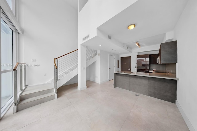 kitchen with light tile patterned flooring, sink, dark brown cabinets, fridge, and a towering ceiling