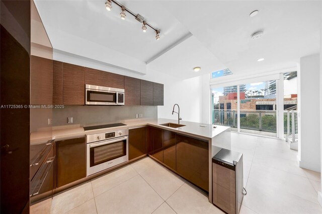 kitchen featuring rail lighting, sink, light tile patterned floors, appliances with stainless steel finishes, and a wall of windows