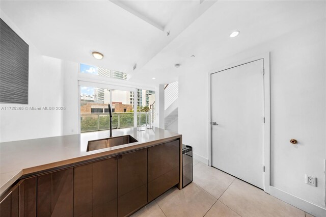 kitchen featuring sink, light tile patterned floors, and dark brown cabinetry