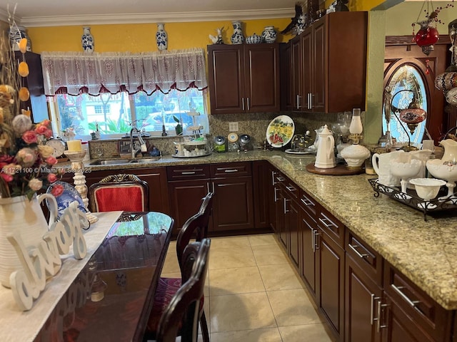 kitchen with tasteful backsplash, sink, light stone countertops, ornamental molding, and light tile patterned floors