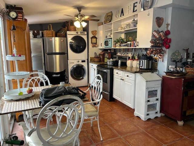 kitchen with ceiling fan, dark tile patterned flooring, stacked washing maching and dryer, appliances with stainless steel finishes, and white cabinets