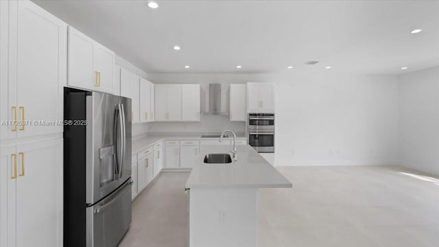 kitchen featuring wall chimney exhaust hood, stainless steel appliances, a kitchen island with sink, white cabinetry, and sink