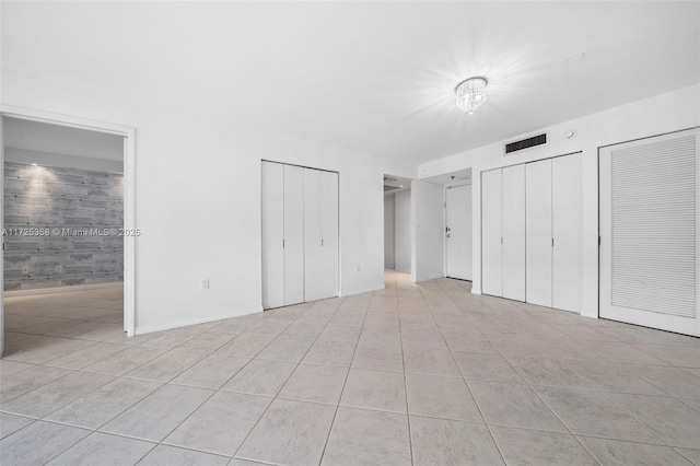 unfurnished bedroom with multiple closets, ensuite bath, and light tile patterned floors