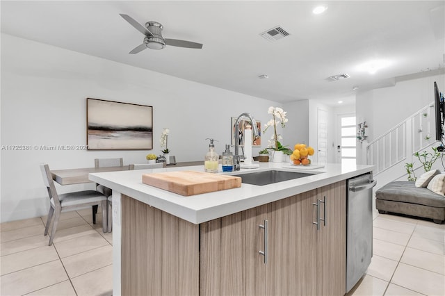 kitchen featuring stainless steel dishwasher, a center island with sink, light tile patterned flooring, ceiling fan, and sink