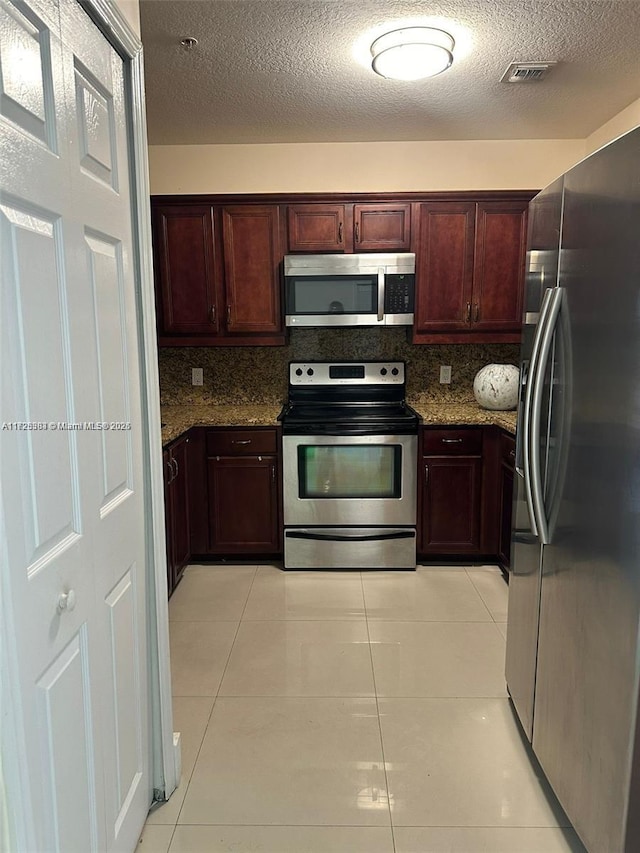 kitchen with appliances with stainless steel finishes, dark stone countertops, tasteful backsplash, and light tile patterned floors