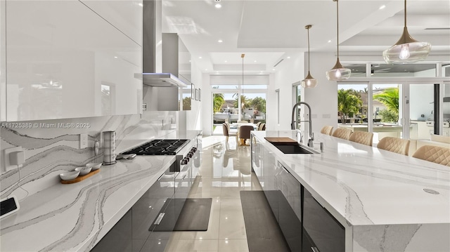 kitchen featuring a large island, range hood, pendant lighting, light stone counters, and sink