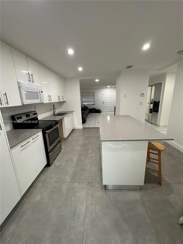 kitchen featuring stainless steel electric stove, a breakfast bar area, a center island, white cabinets, and sink