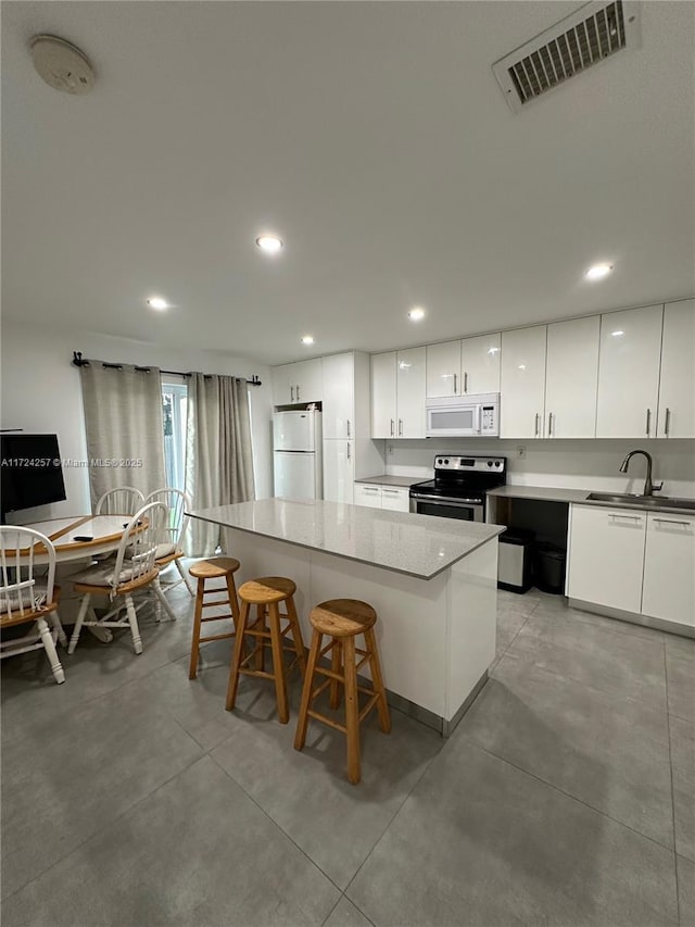 kitchen featuring white appliances, a kitchen breakfast bar, white cabinetry, and a kitchen island